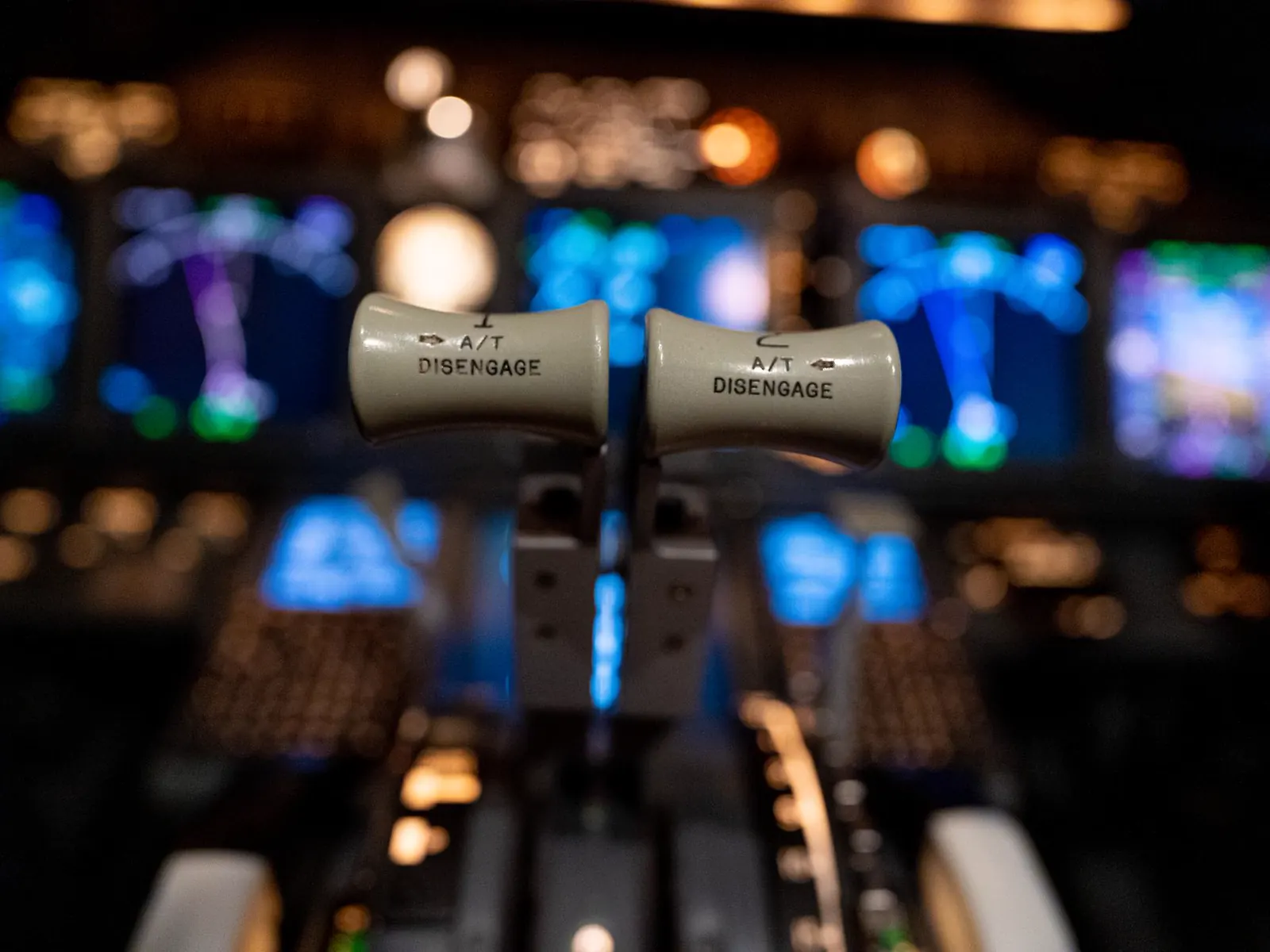 An aircraft cockpit at night, instrument panels and autothrottle levers lit in the foreground.