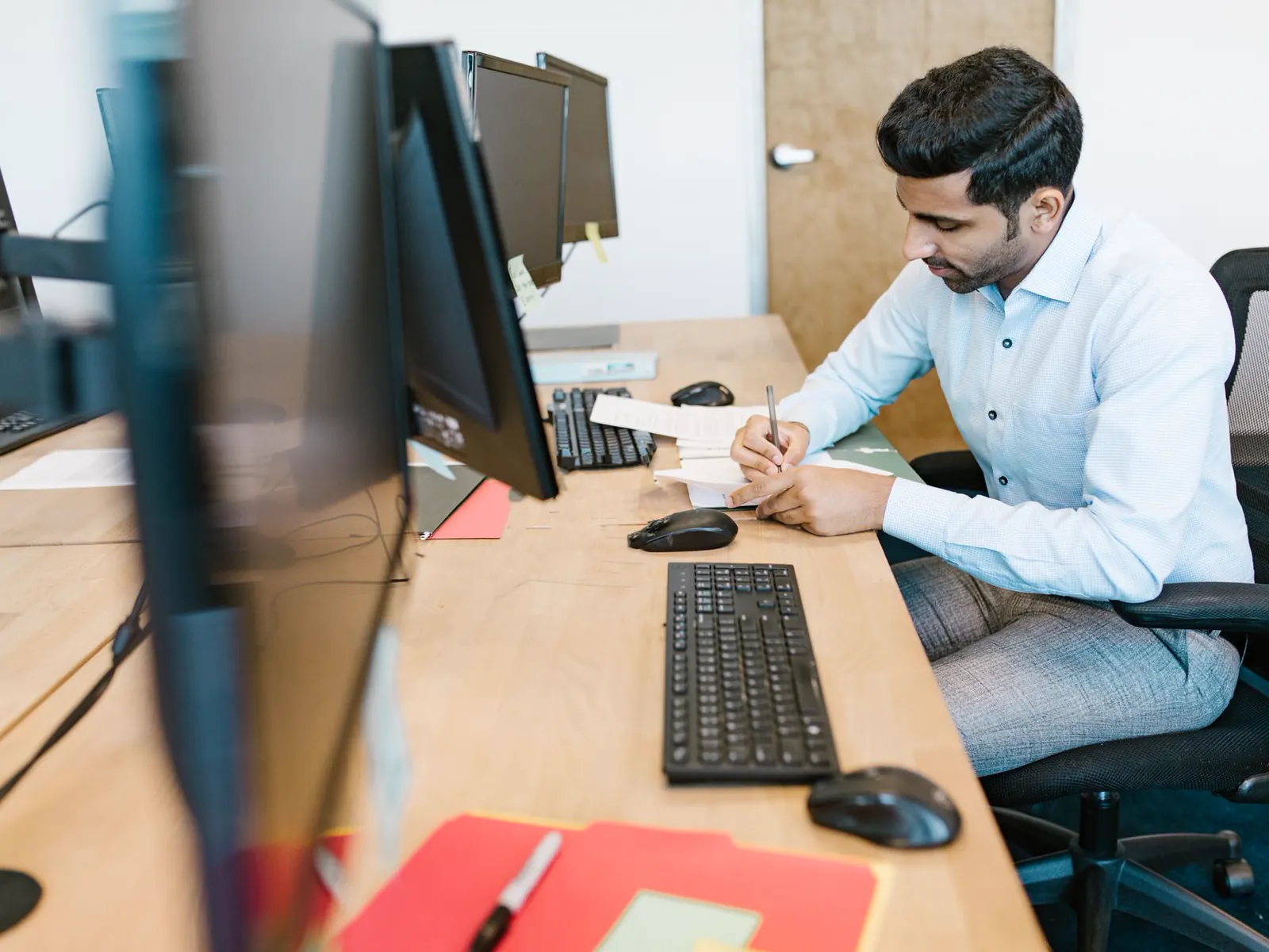 An engineer making notes at a desk beside a computer monitor and keyboard.