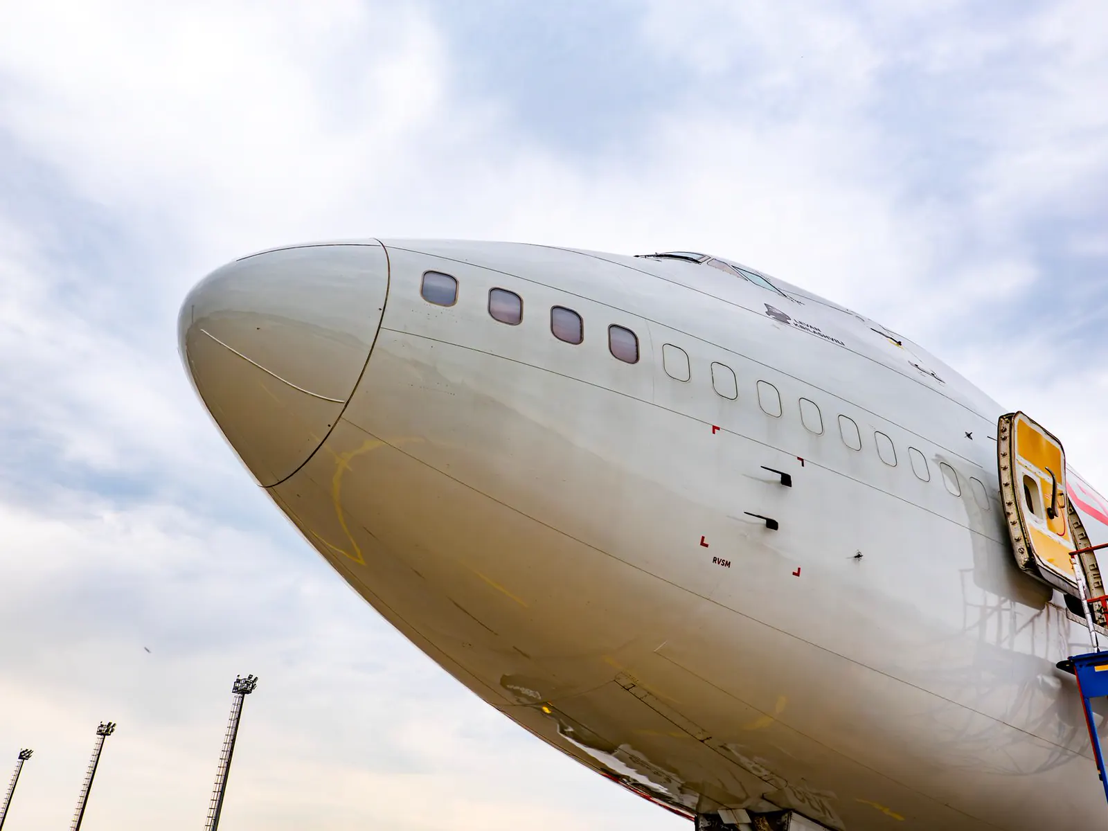 The nose of a retired airliner standing on hard standing, an access hatch open behind the flight deck windows.