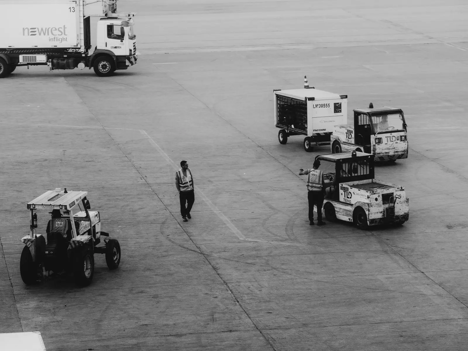 Airport ground crew moving service vehicles on an apron, in black and white.