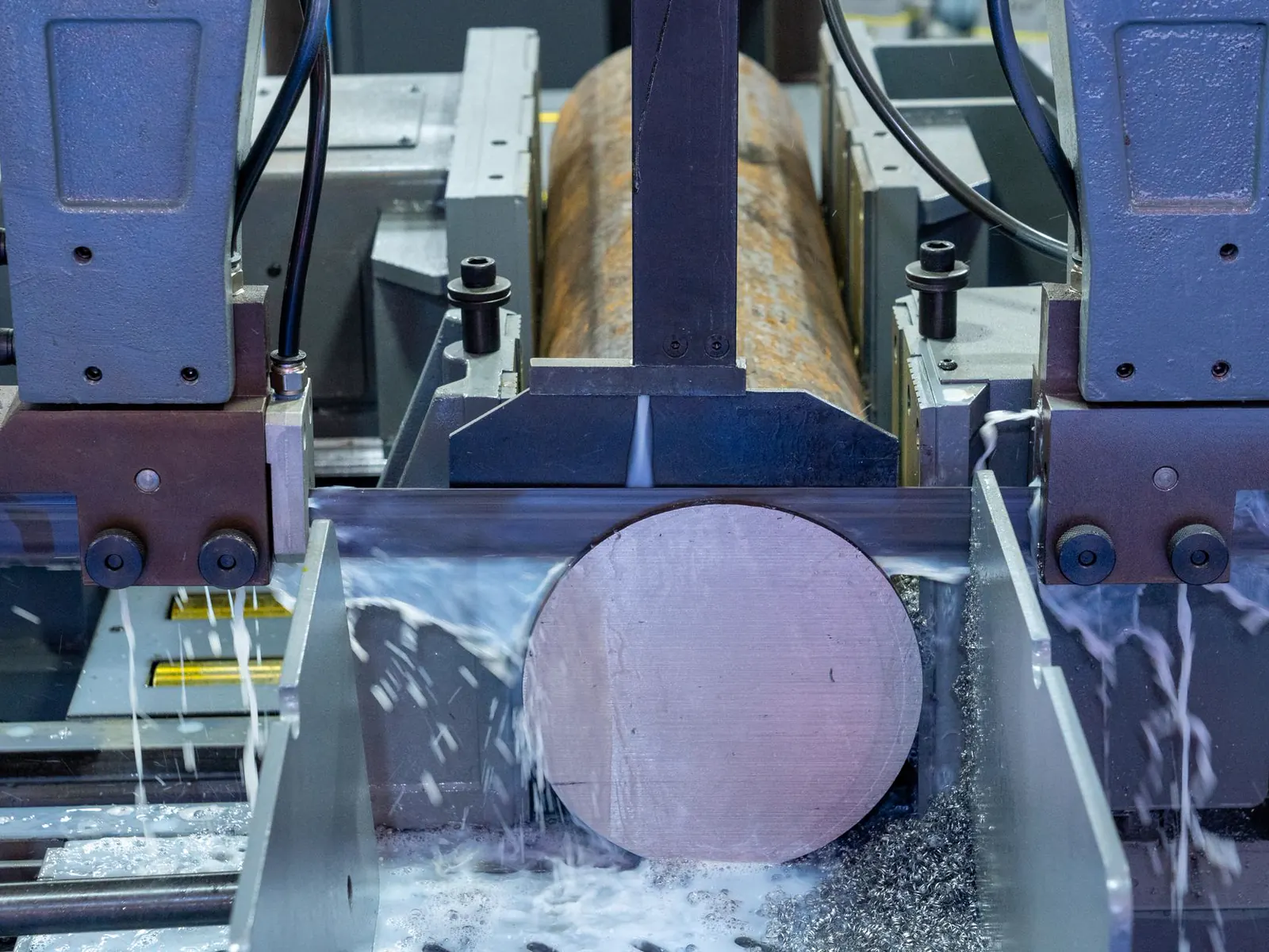 A metal bar clamped in a machine tool being cut to size, coolant running over the work.