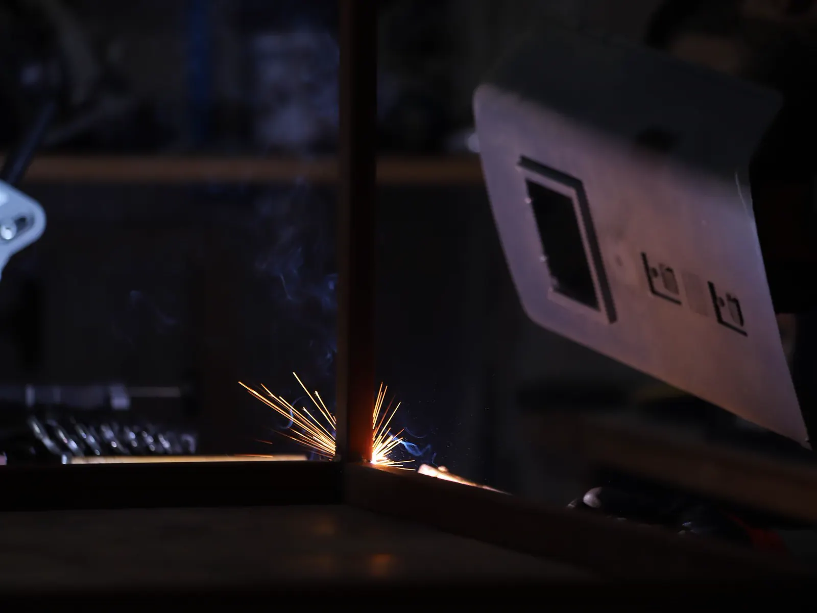 A welding arc in a dark workshop, sparks across the frame.